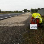 Sac à dos, veste haute-visibilité jaune fluo et pancarte d'auto-stop à destination de Lyon